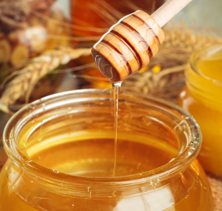 Honey drips from a honey spoon into a jar of honey.